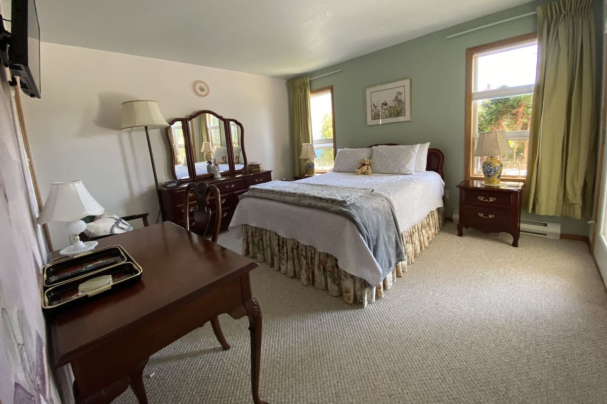 Een slaapkamer met een bed, een kaptafel, een bureau en een raam met gordijnen.