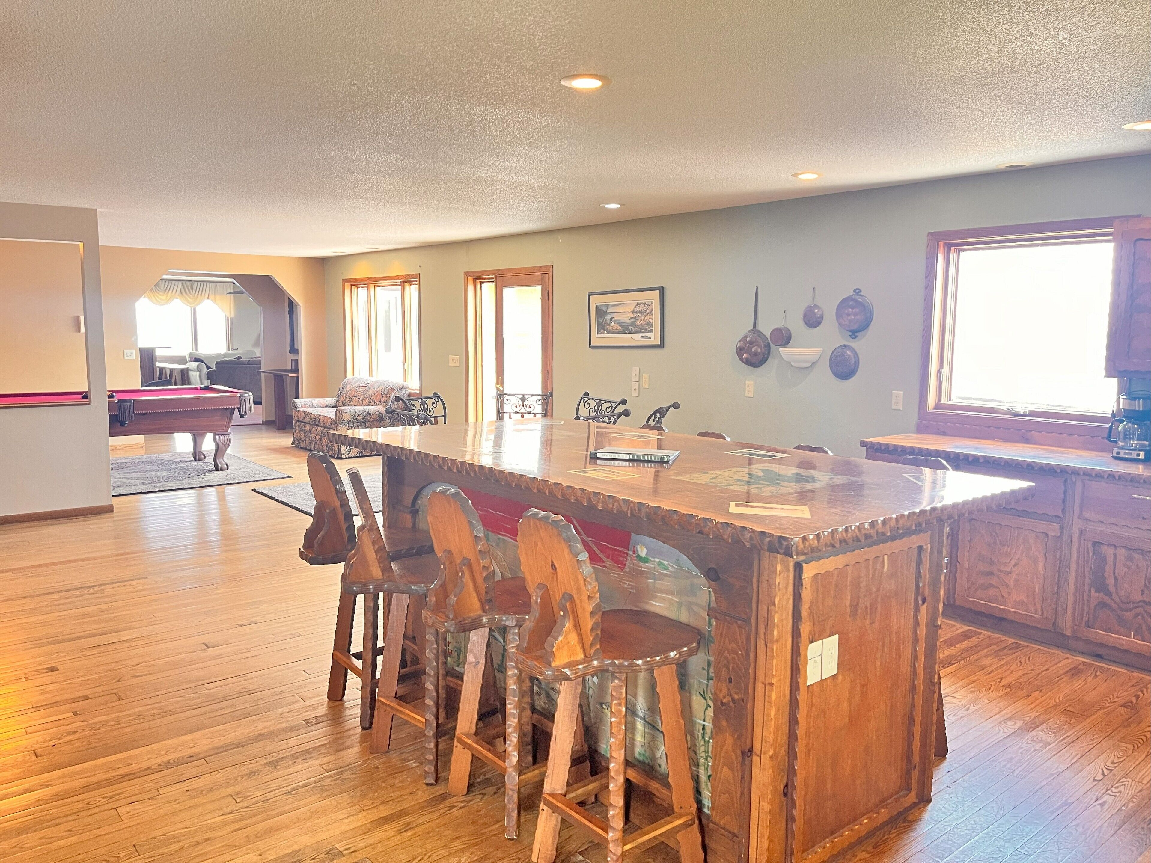 A spacious living area with a wooden pool table, a dining table with chairs, and a kitchen area with wooden cabinets.