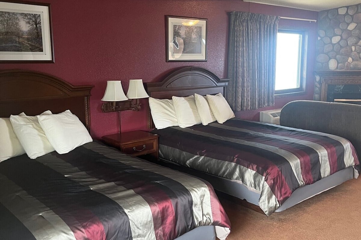 A hotel room with two beds, a stone fireplace, and a large window with curtains.
