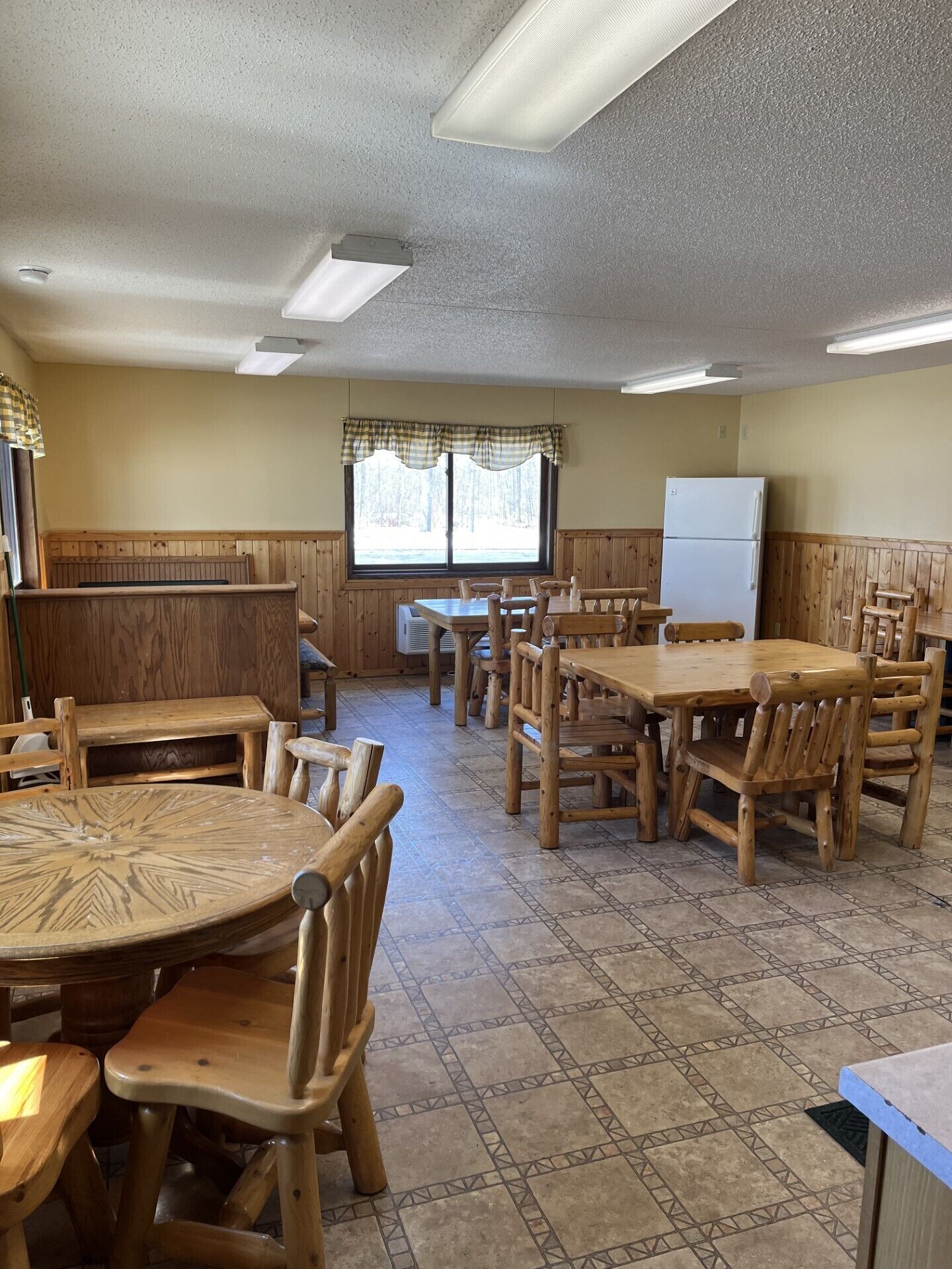Un restaurante con cabinas y mesas de madera, un refrigerador blanco y una ventana con adornos escoceses.