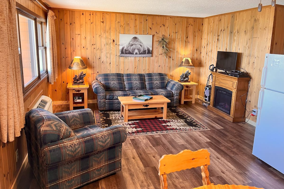 A cozy living room with a plaid sofa, a wooden coffee table, and a fireplace.