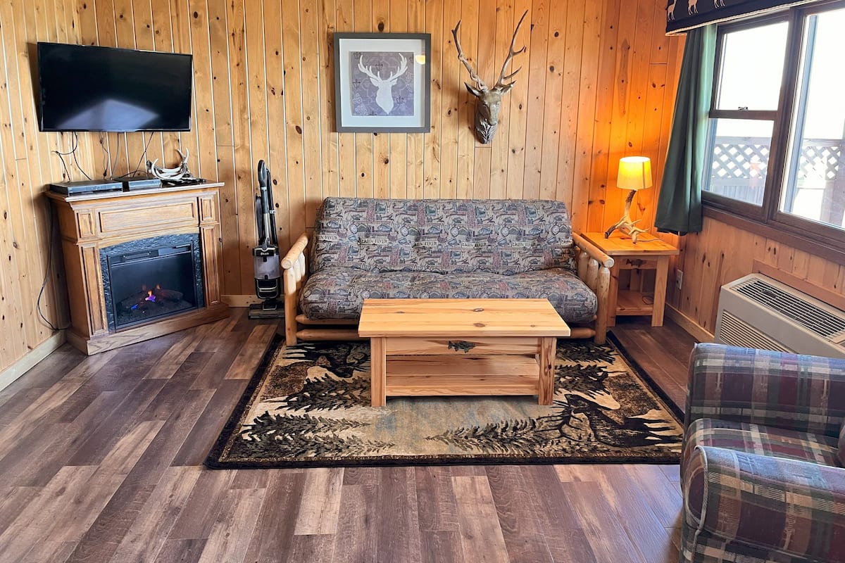 A cozy living room with a fireplace, a sofa, a coffee table, a TV, and a mounted deer head.