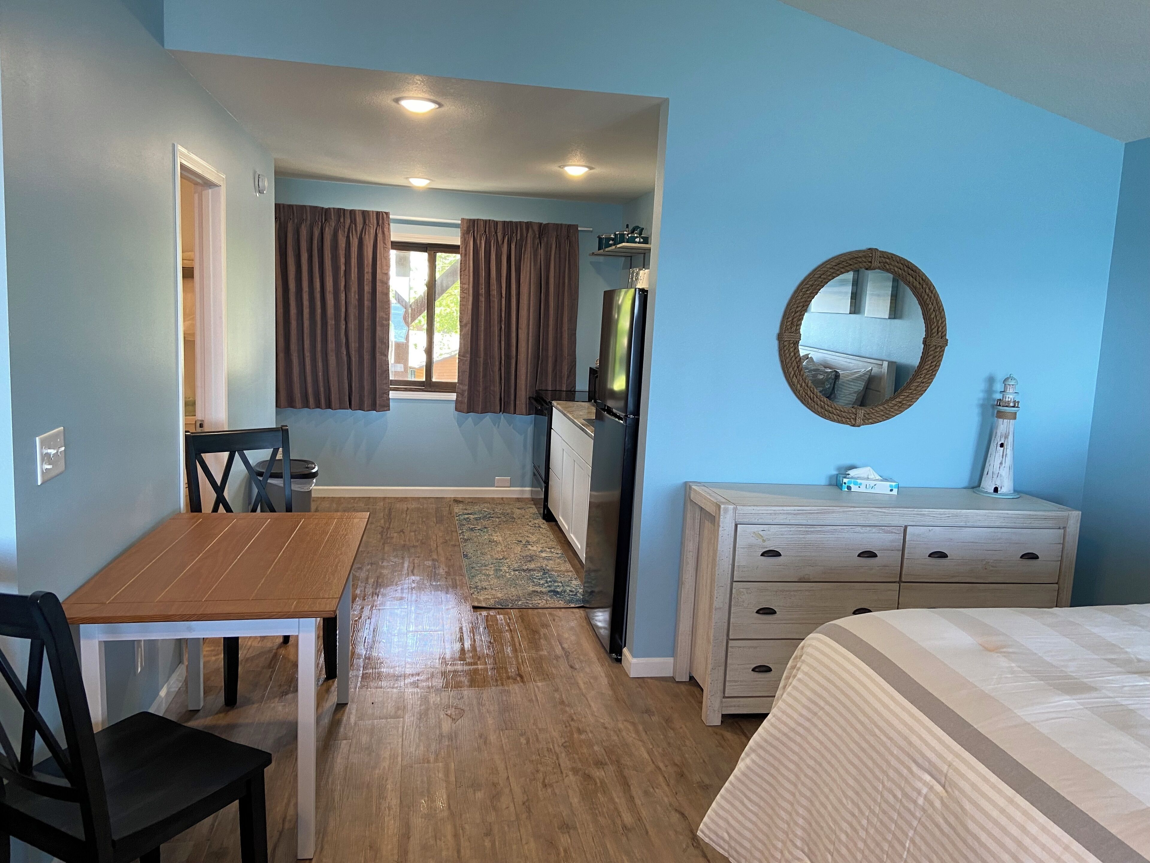 Una habitación pequeña con una mesa de comedor de madera, una silla, una cama, un aparador y un espejo.
