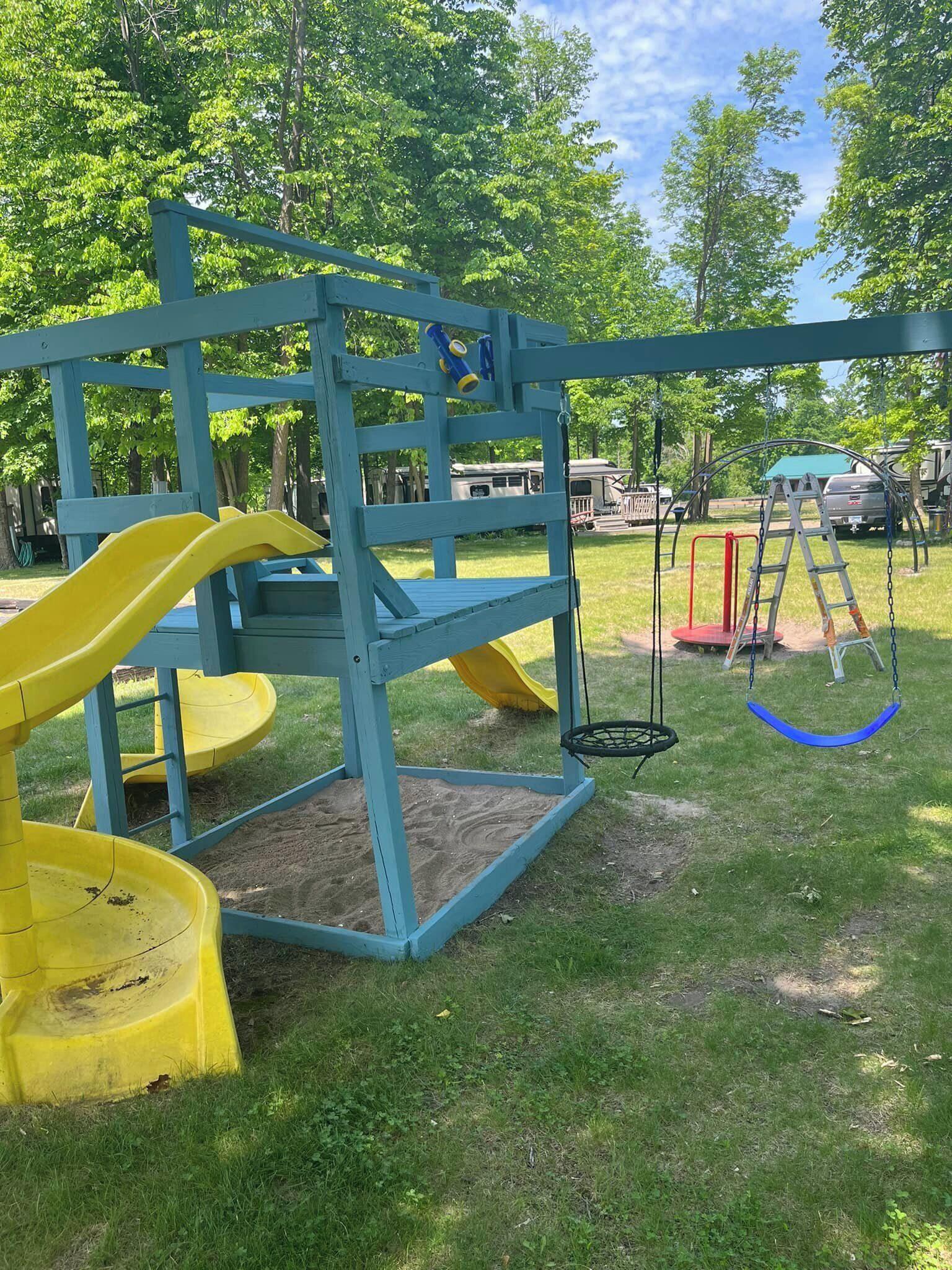 A playground with a slide, swings, and a ladder.