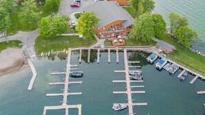 An aerial view of a marina with multiple docks and boats, a building with a porch, and a grassy area with trees. - Horseshoe Bay Lodge (Walker)