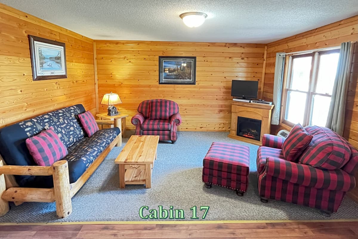 A cabin with a wooden interior, a sofa, a chair, a small table, and a fireplace.