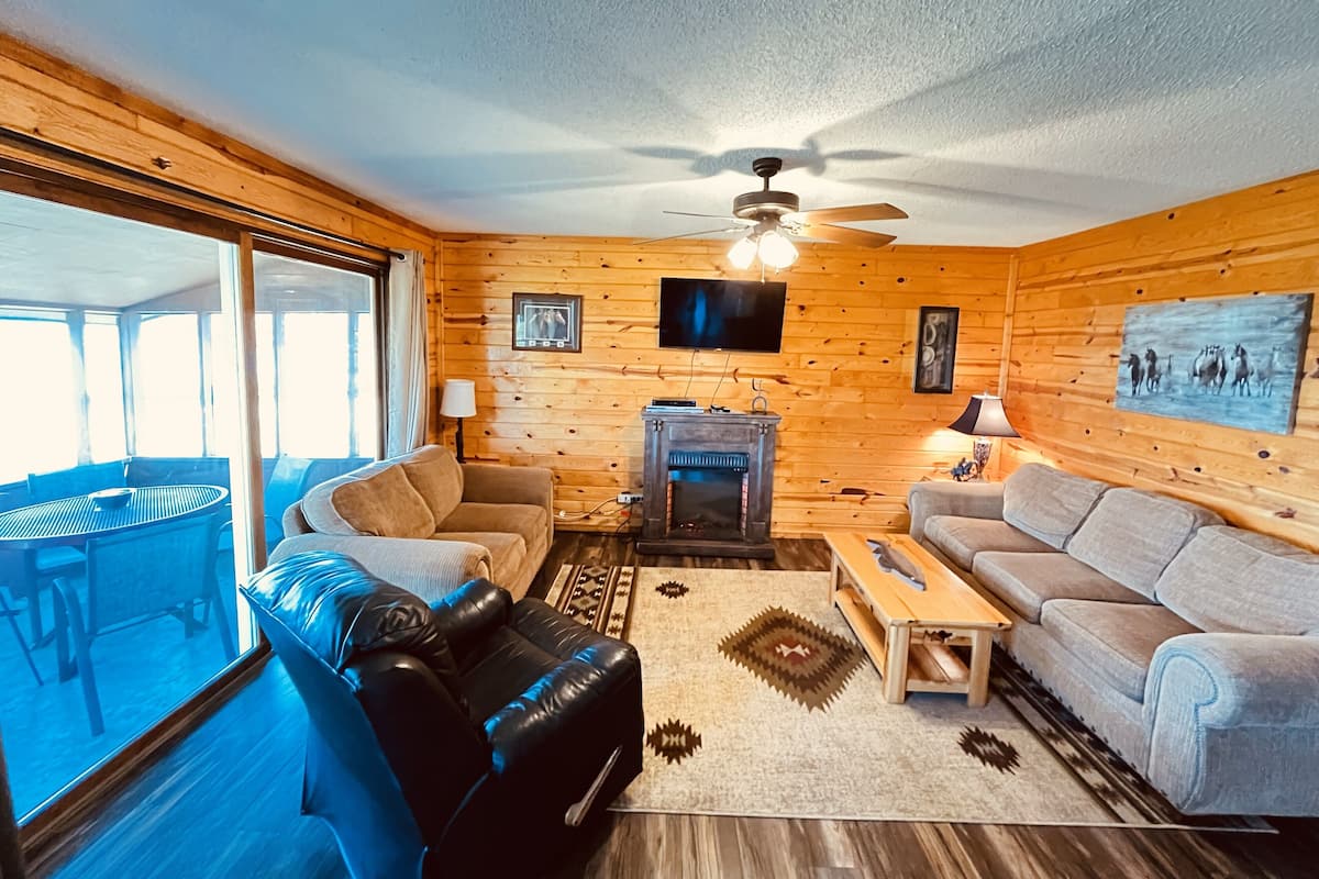 A cozy cabin interior with a fireplace, two sofas, a coffee table, and a ceiling fan.