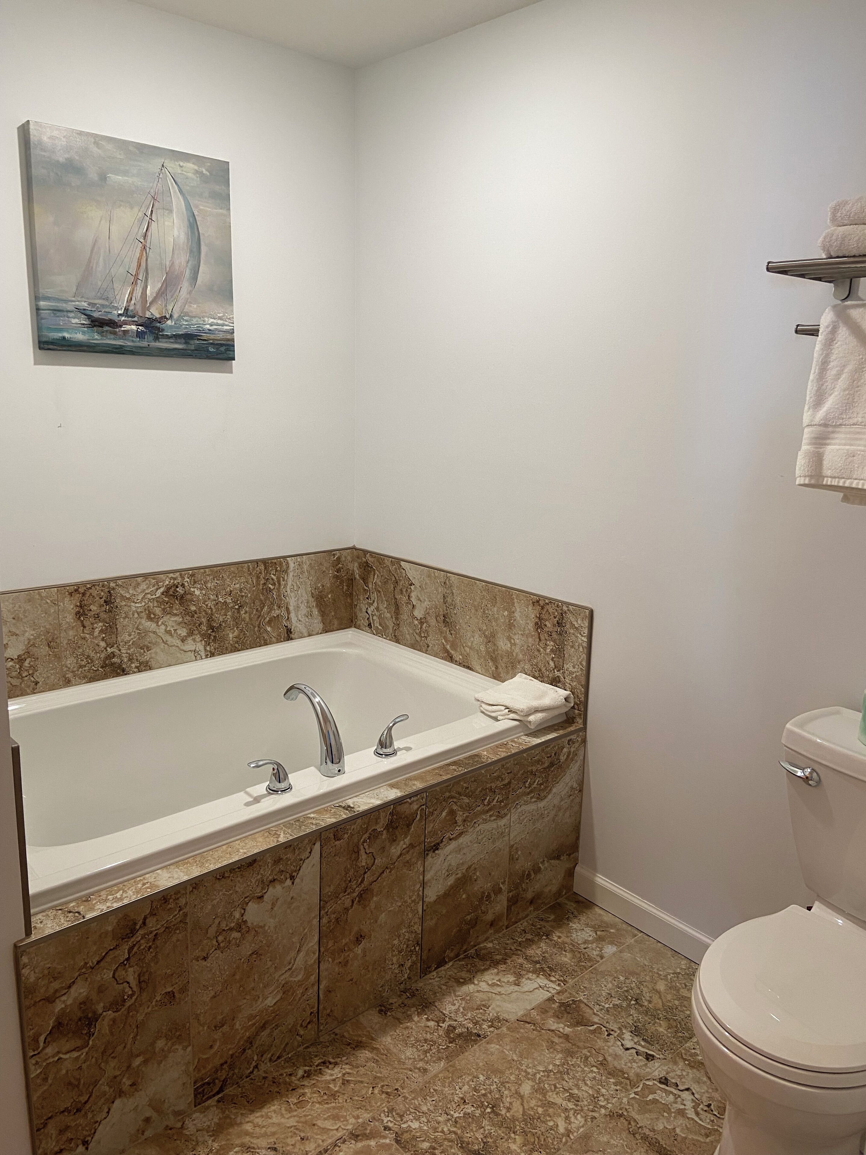 Un baño con una bañera grande, un inodoro y un cuadro de un velero en la pared.