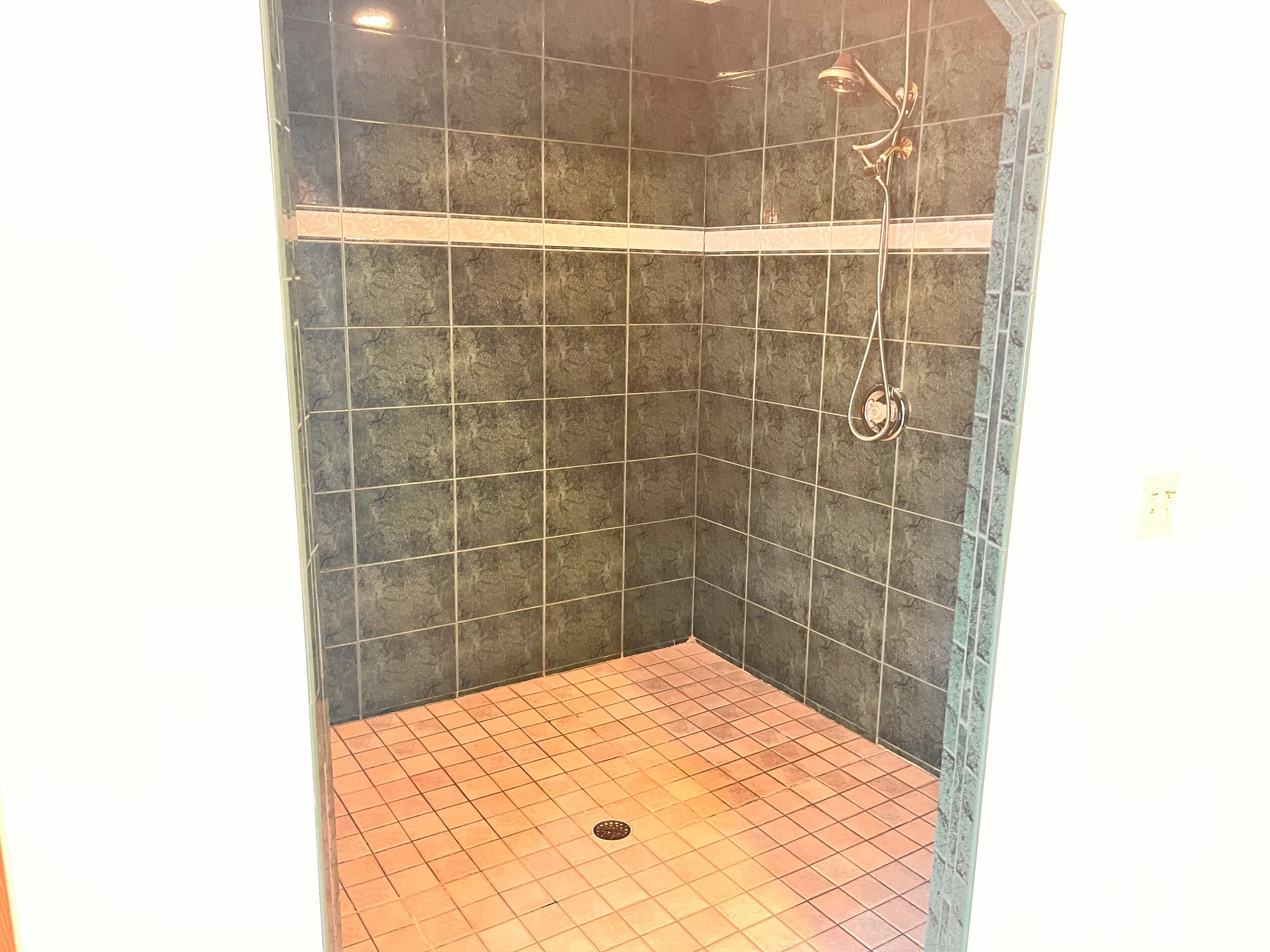 Ducha con azulejos oscuros y un desagüe en el centro.