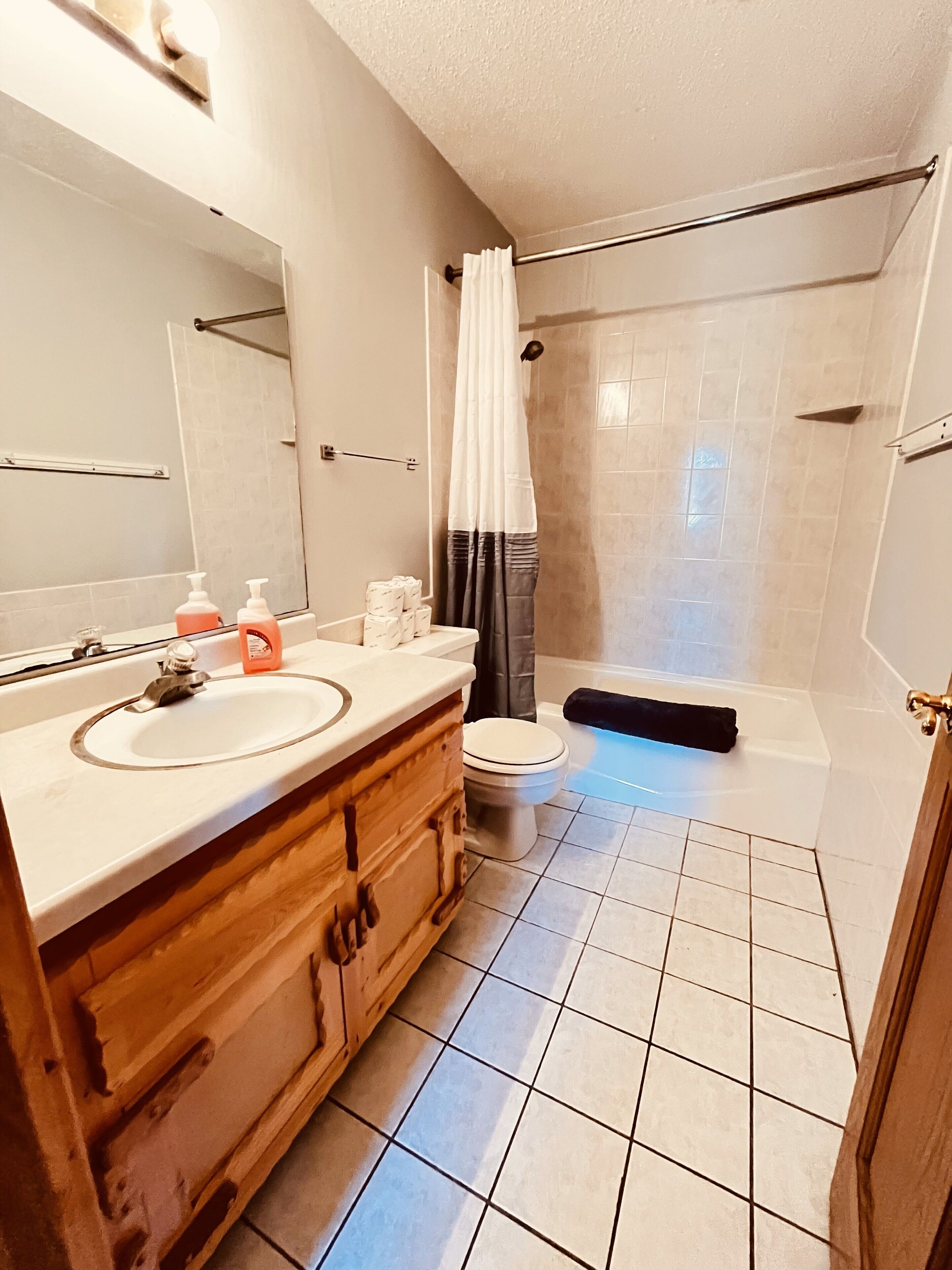 Ein Badezimmer mit einem Holzlagerfläschchen, einem weißen Waschbecken, einem Spiegel, einer Toilette, einer Duschkabine mit Vorhang und einer Badewanne.
