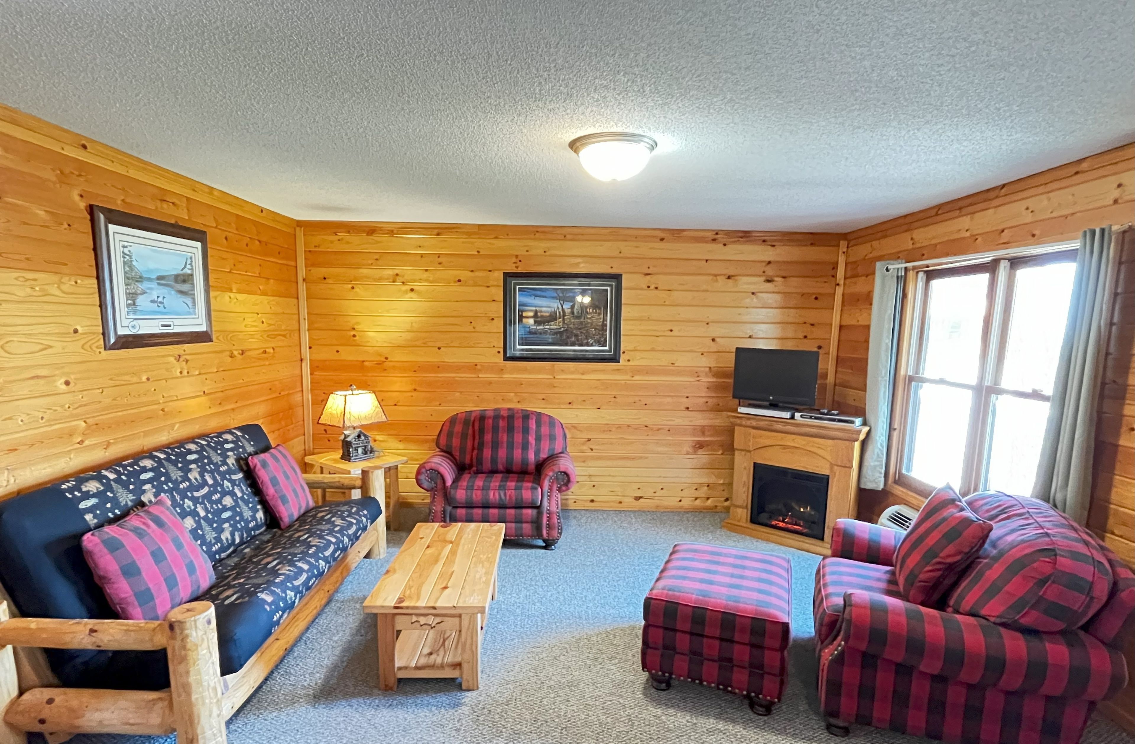 A cabin with a wooden interior, a sofa, a chair, a small table, and a fireplace.