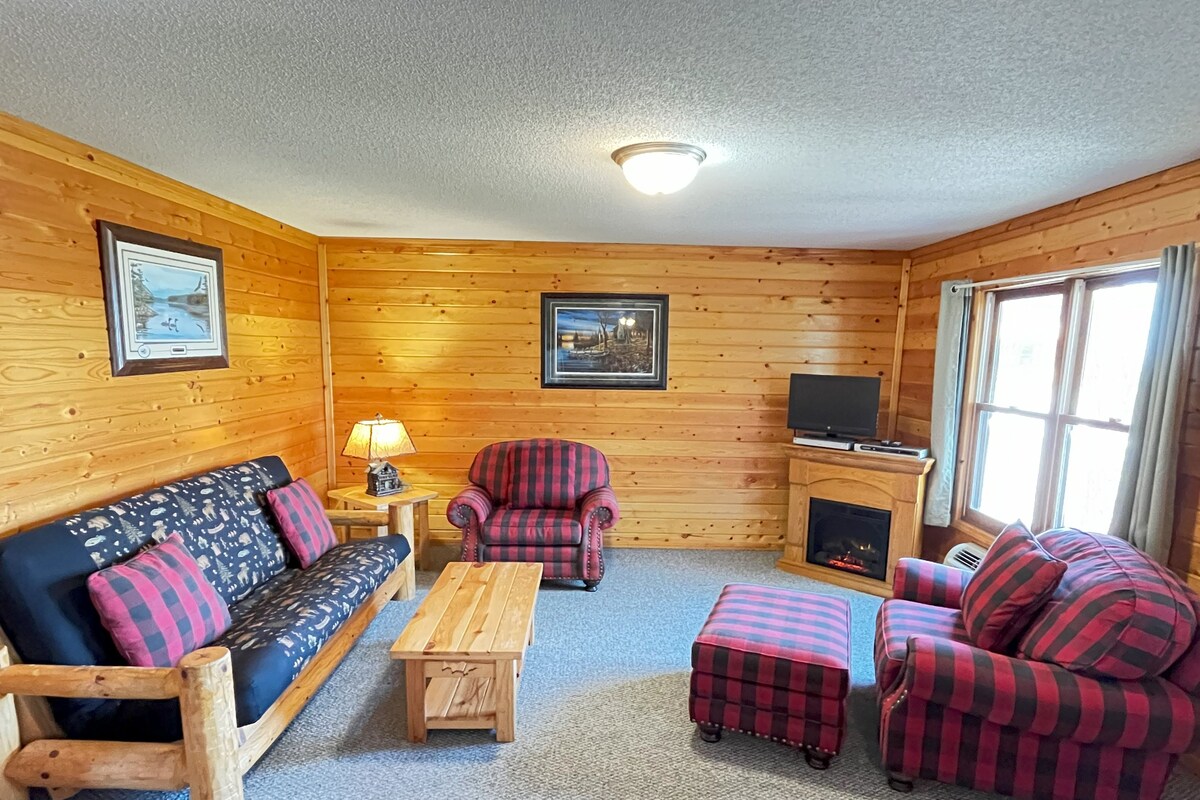A cabin with a wooden interior, a sofa, a chair, a small table, and a fireplace.