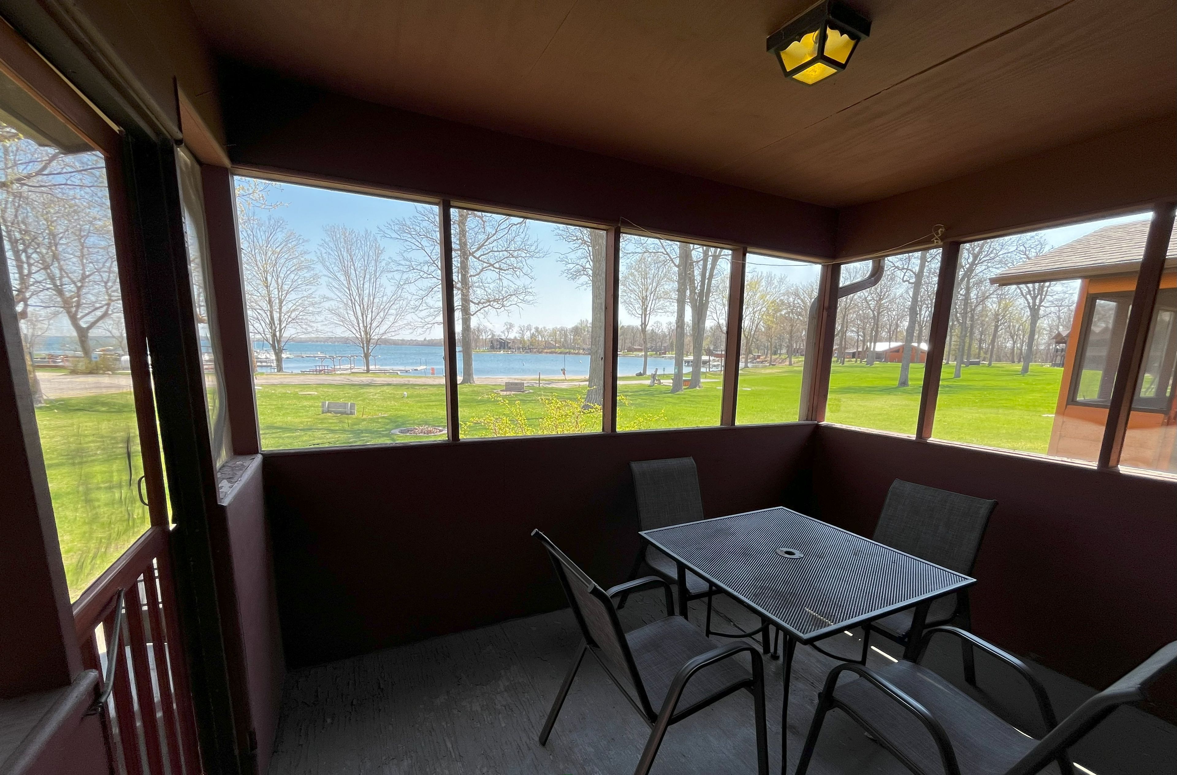 Une cabane équipée d’une table et de chaises, avec de grandes fenêtres donnant sur une zone herbeuse et un plan d’eau.
