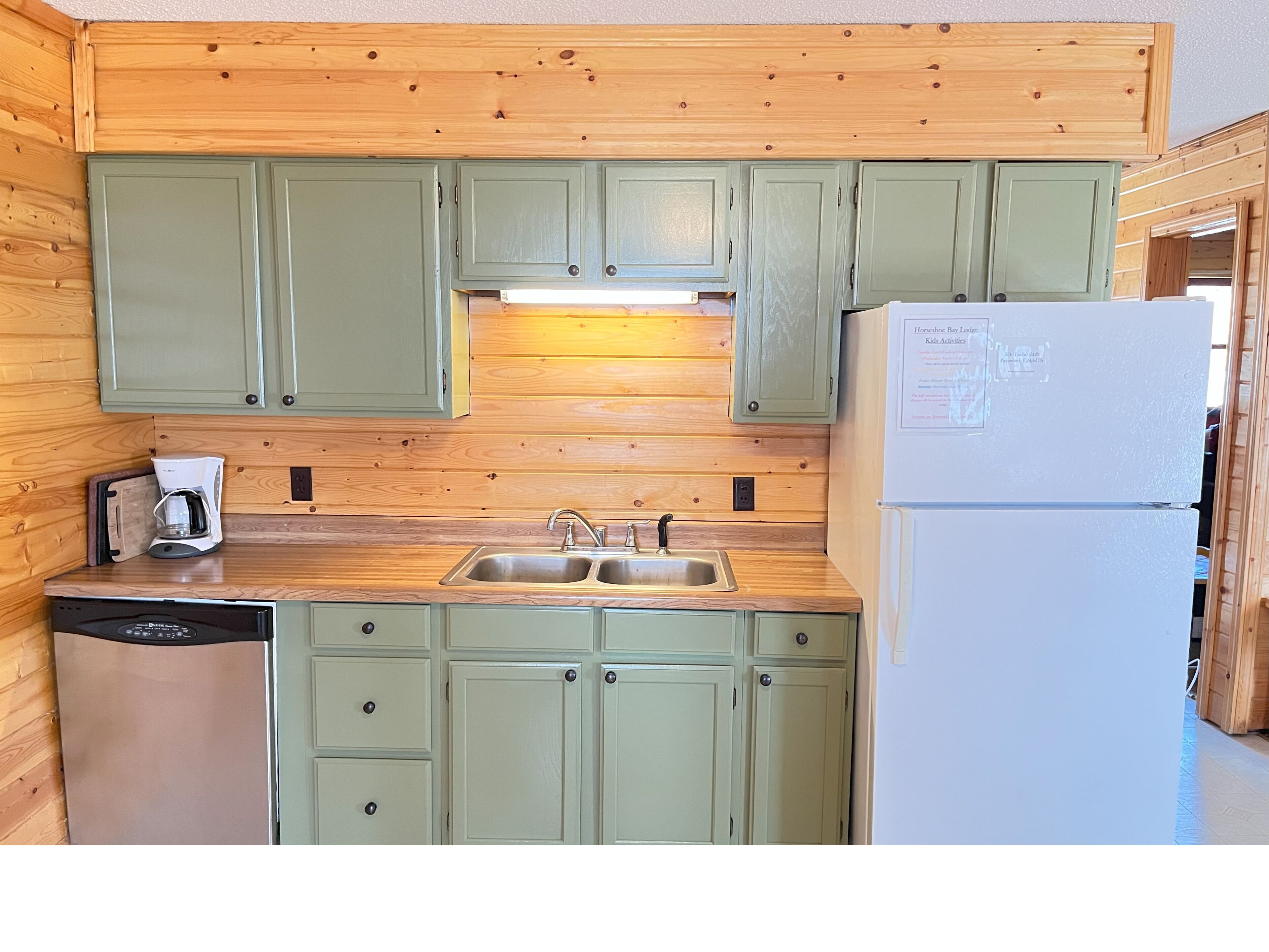 A compact kitchen with green cabinets, a sink, a coffee maker, and a refrigerator.
