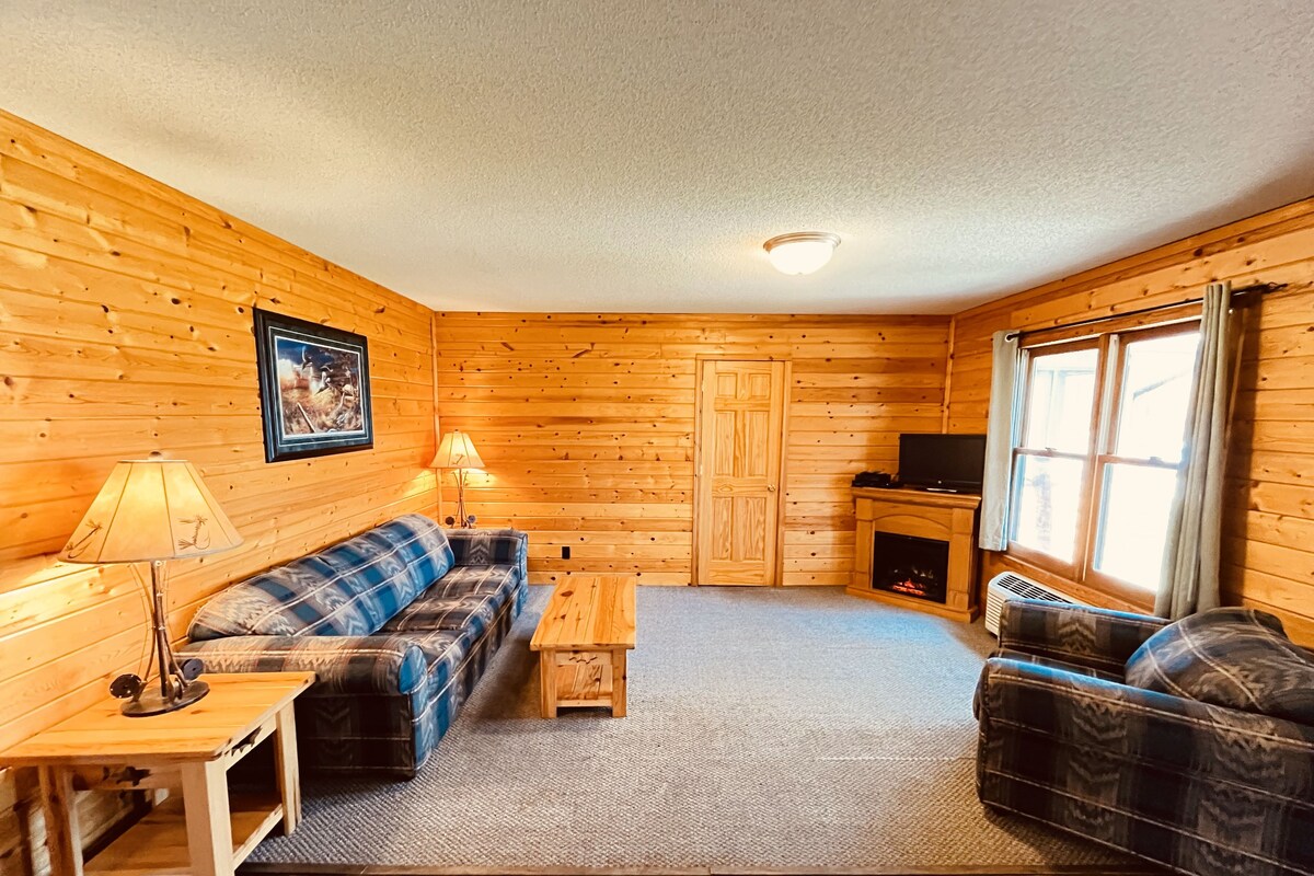 A cabin with wooden walls, a sofa, a coffee table, a TV, and a fireplace.
