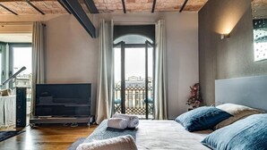 A modern hotel room with a large bed, a flat-screen TV, and a balcony with a city view. - Godó Luxury Apartment Passeig de Gracia (Barcelona)