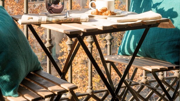 A balcony with a table set for a meal, featuring a cup, a plate with croissants, and a vase with flowers. - Godó Luxury Apartment Passeig de Gracia (Barcelona)