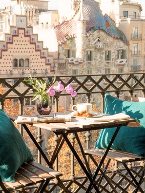 Un balcón con una mesa dispuesta para una comida, que incluye una taza, un plato con croissants y un jarrón con flores.