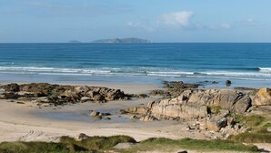 A coastal beach with rocky outcrops and a distant island. - Pousada A Lanzada (O Grove)