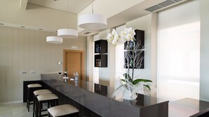 A modern kitchen with a long island counter, bar stools, pendant lighting, and a decorative orchid arrangement. - Pousada A Lanzada (O Grove)