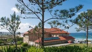 A large stone building with a red roof, surrounded by pine trees and a view of the sea. - Pousada A Lanzada (O Grove)