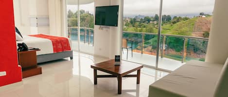 A hotel room with a bed, a sofa, a TV, and a balcony with a view of the landscape.