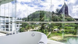 A modern hotel room with a large glass window overlooking a scenic view of a hill and a body of water. - Hotel Los Recuerdos (Guatapé)