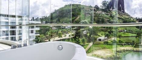 Una habitación de hotel moderna con un amplio ventanal que ofrece una vista panorámica de una colina y una masa de agua.