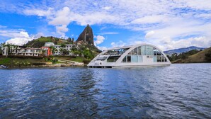 A modern houseboat with a curved roof and large windows, floating on a calm body of water. - Hotel Los Recuerdos (Guatapé)