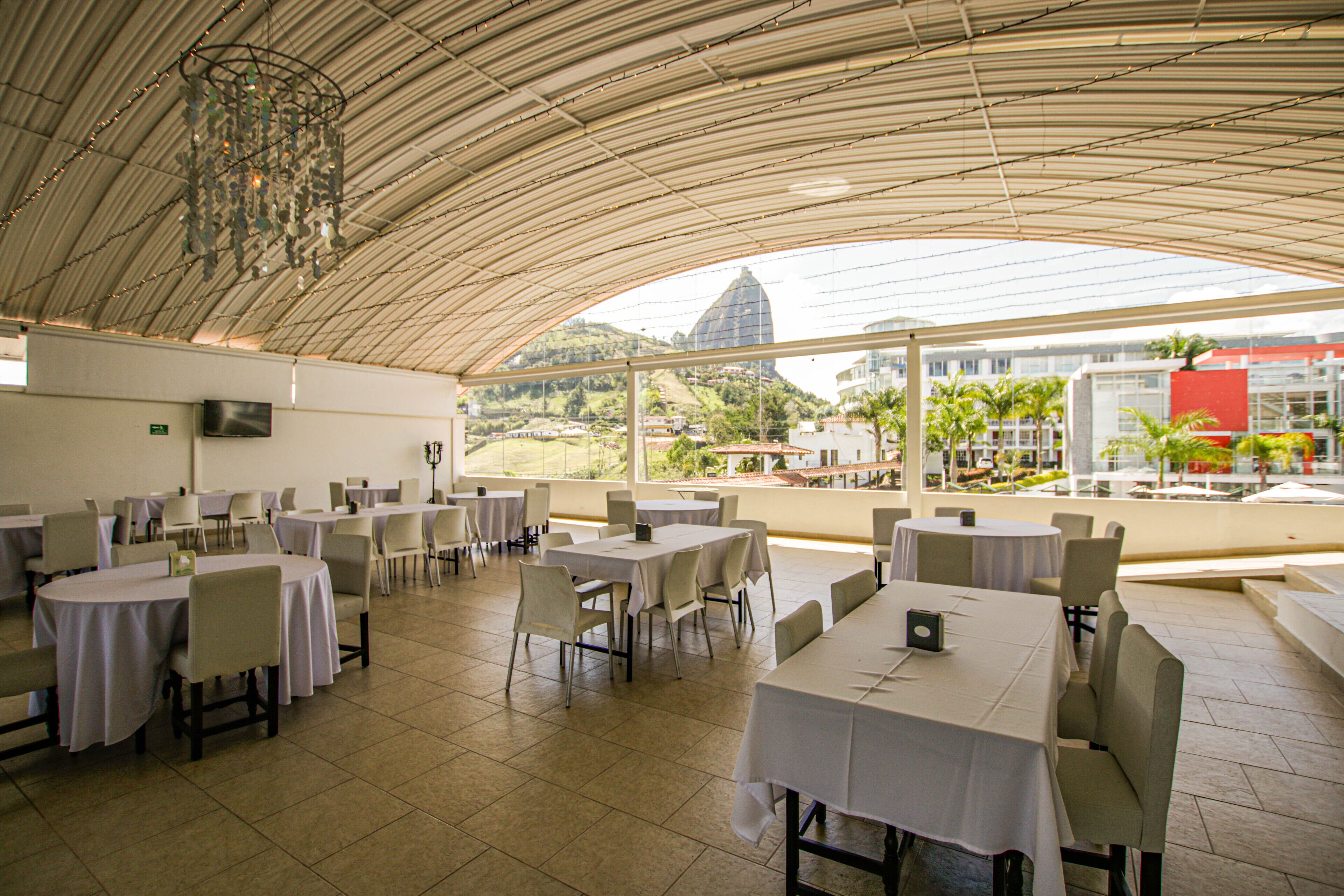 A spacious indoor dining area with multiple tables and chairs, large windows offering a view of the cityscape and a mountain in the distance.