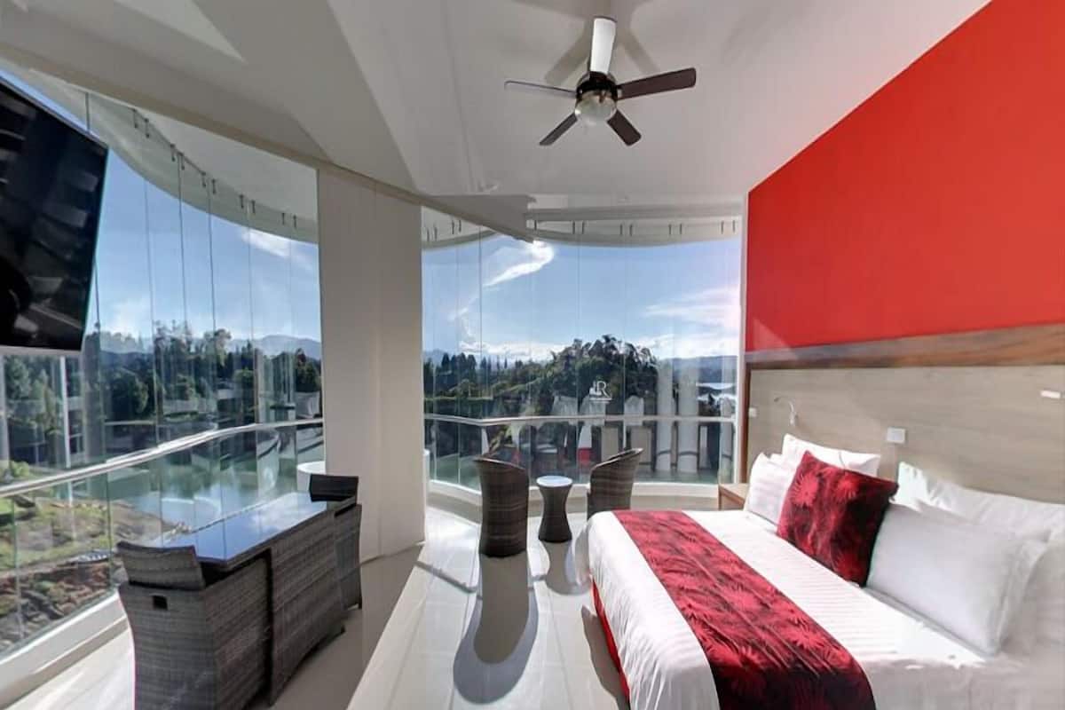 A modern bedroom with a large bed, a glass balustrade, and a view of a mountainous landscape.
