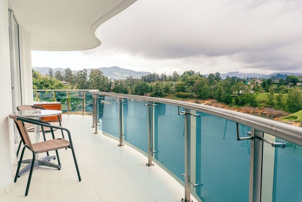 A balcony with a glass railing overlooking a river and mountains. - Hotel Los Recuerdos (Guatapé)