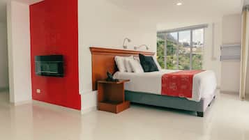 Une chambre moderne avec un lit, un téléviseur fixé au mur et une fenêtre donnant sur un paysage verdoyant.