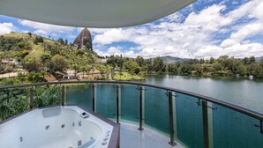 A balcony with a hot tub overlooking a lake, surrounded by lush greenery and a mountainous backdrop. - Hotel Los Recuerdos (Guatapé)