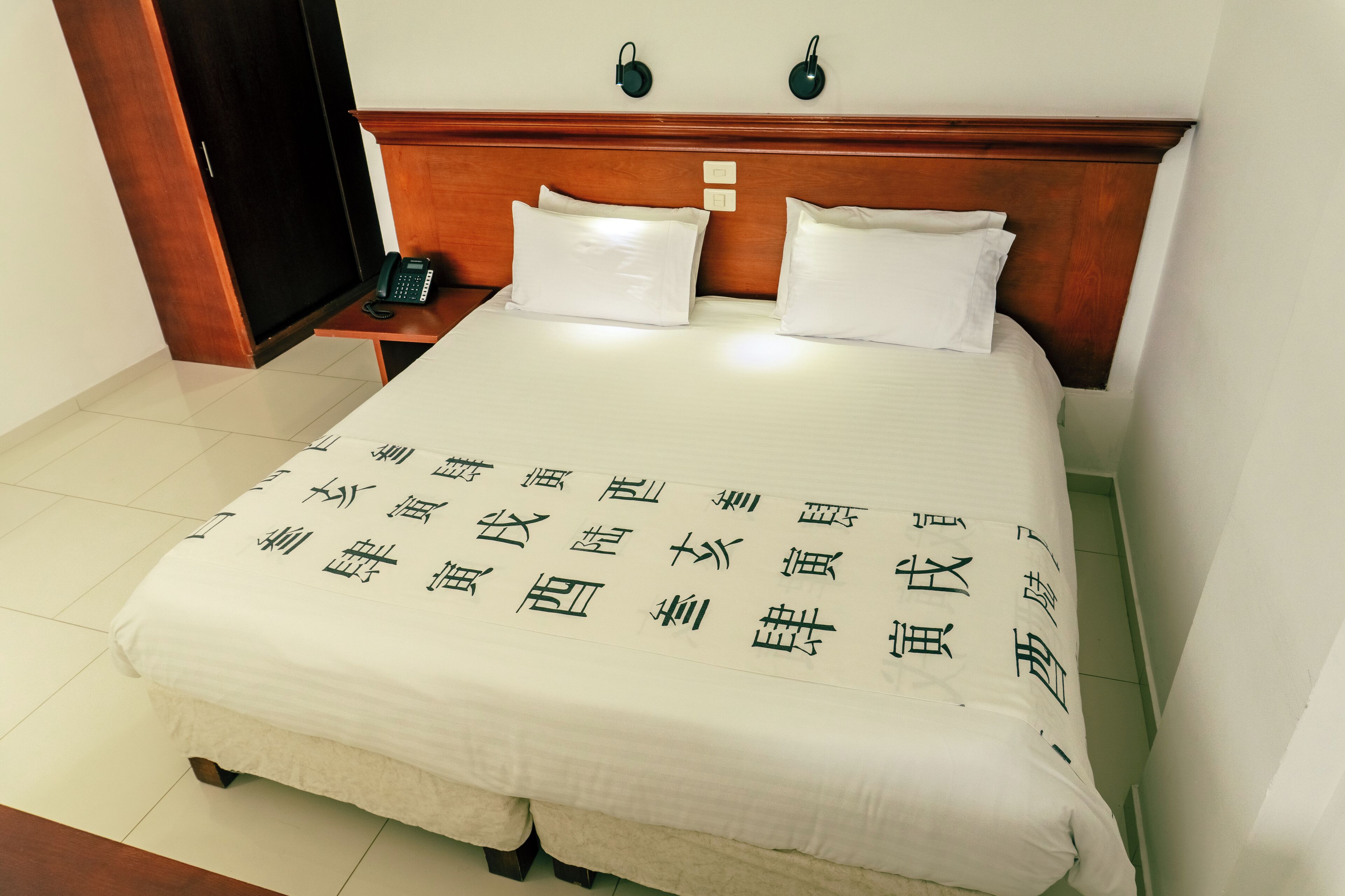 A hotel room with a neatly made bed, a wooden headboard, bedside tables, and a telephone.