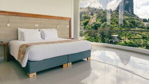 A bedroom with a large bed, wooden headboard, and a view of a mountain. - Hotel Los Recuerdos (Guatapé)
