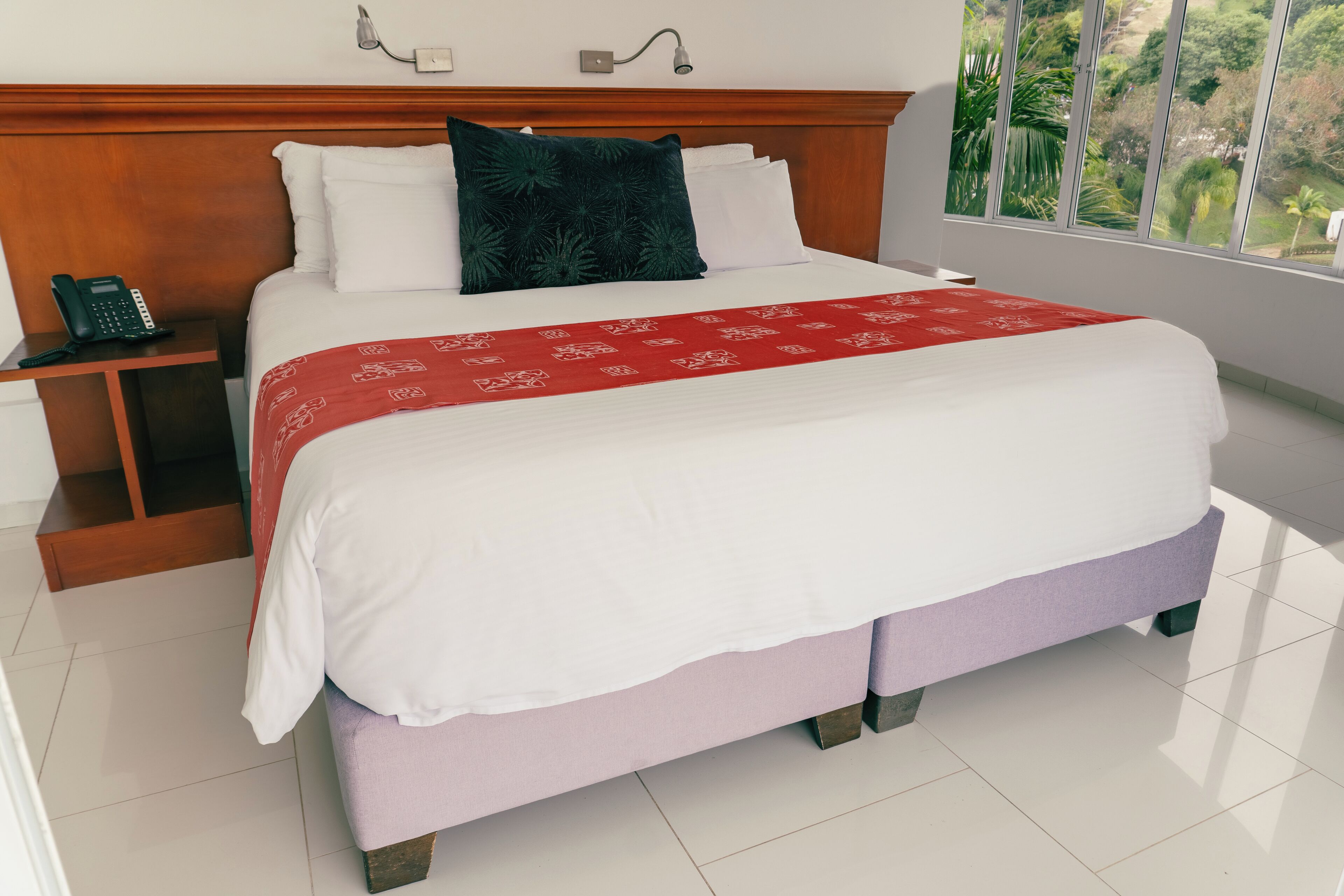 A neatly made bed with a red and white patterned bedspread, a dark green pillow, and a wooden headboard.