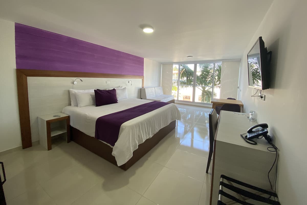 A hotel room with a large bed, bedside tables, a desk with a phone, and a TV mounted on the wall.