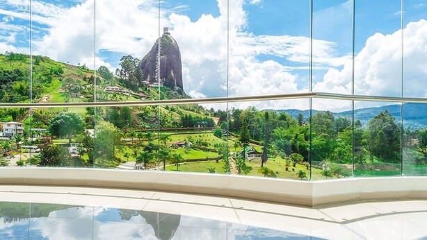 A view from a high-rise building with a glass facade, overlooking a lush green landscape with a prominent rock formation. - Hotel Los Recuerdos (Guatapé)
