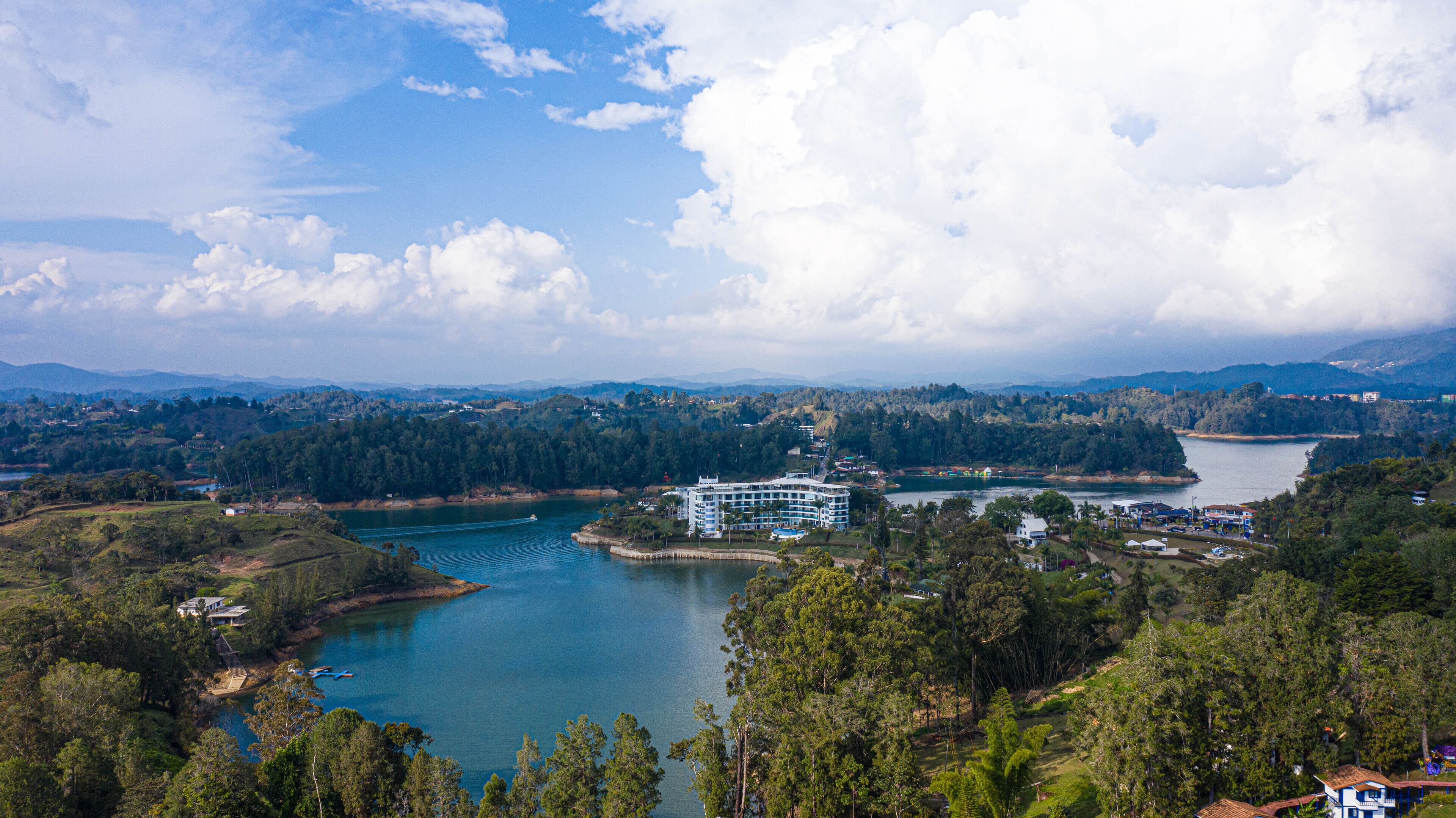 Un resort con un edificio grande que domina un lago, rodeado de bosque denso y colinas.