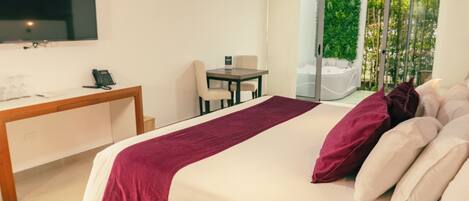 A hotel room with a bed, a desk with a telephone, a chair, a table, and a TV mounted on the wall.