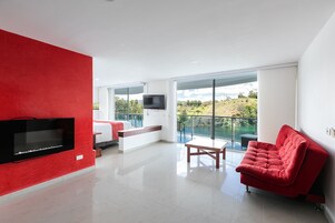 Una sala moderna con una pared de acento roja, un televisor de pantalla plana, un sofá y un balcón con vistas al campo.