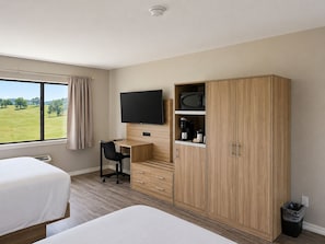 Une chambre dâhĂŽtel avec deux lits, un bureau avec une chaise, une tĂ©lĂ©vision, une armoire et une vue sur un champ verdoyant.