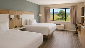 A hotel room with two beds, a desk, a chair, a lamp, and a view of the outdoors. - Oak Ridge Inn (Plymouth)