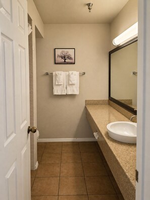 A bathroom with a white door, a framed picture of a tree, two towels on a rack, a sink, and a mirror. - Oak Ridge Inn (Plymouth)