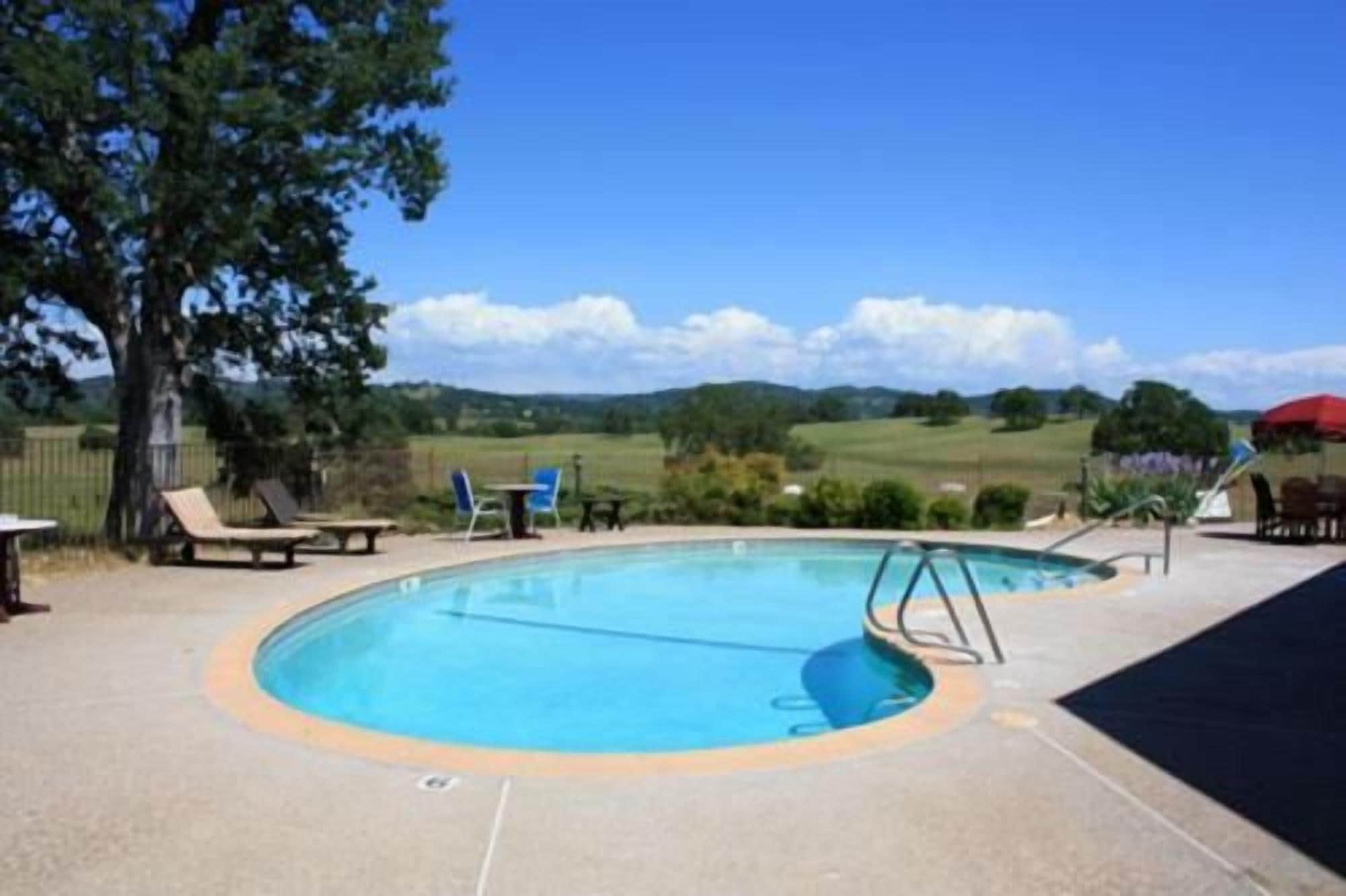 Una piscina con una terraza circundante, algunas sillas de descanso y vistas al campo.