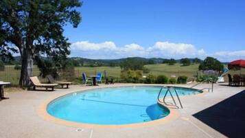 Una piscina con una terraza circundante, algunas sillas de descanso y vistas al campo.