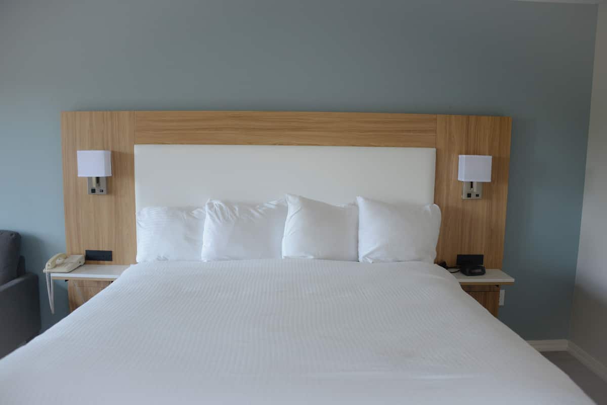 A large bed with white linens, two bedside tables with lamps, and a wooden headboard.