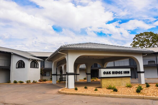 The exterior of Oak Ridge Inn, featuring a covered entrance with arches, a tiled roof, and a landscaped area with small plants.
