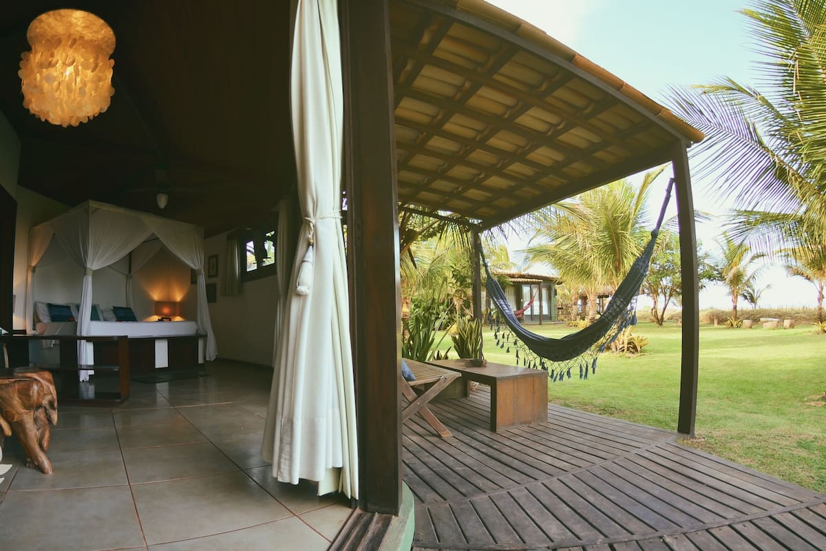 A covered outdoor seating area with a wooden deck, a hammock, and a canopy bed.